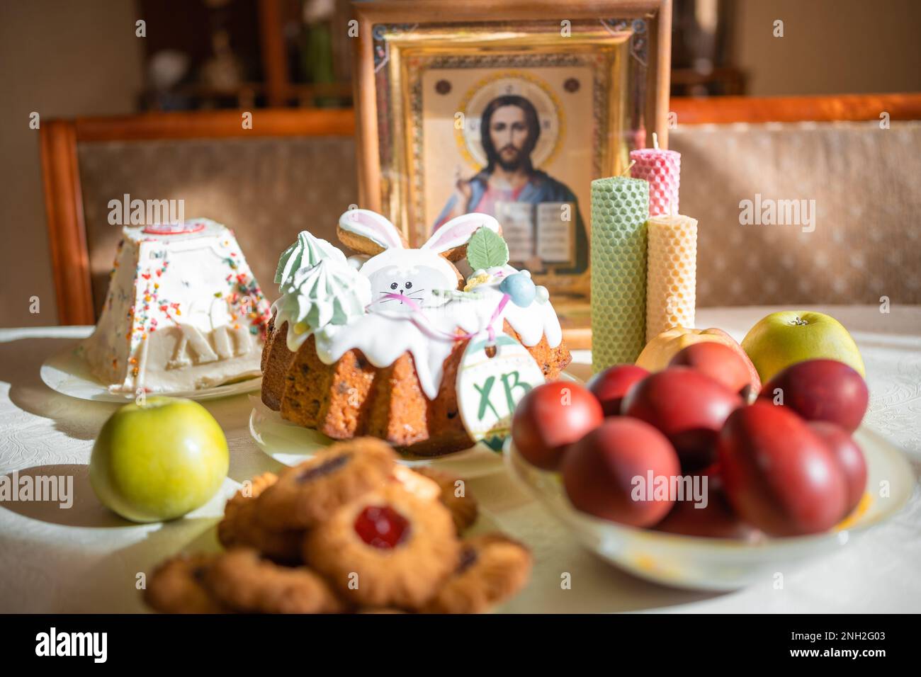 Gâteau de Pâques avec œufs peints, pommes et biscuits sur la table dans la cuisine. Icônes de l'église et bougie en arrière-plan. Thème de la religion orthodoxe. Banque D'Images