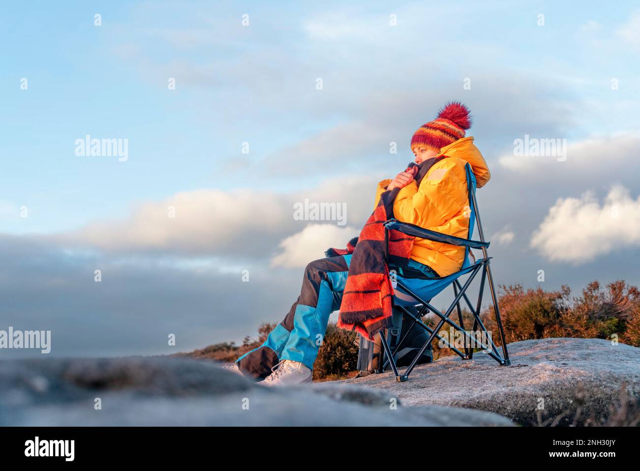 Femme en manteau jaune et foulard orange atteignant la destination et assis sur des chaises de plage au sommet d'une colline ou d'une montagne au lever du soleil. Hiver froid britannique. Banque D'Images
