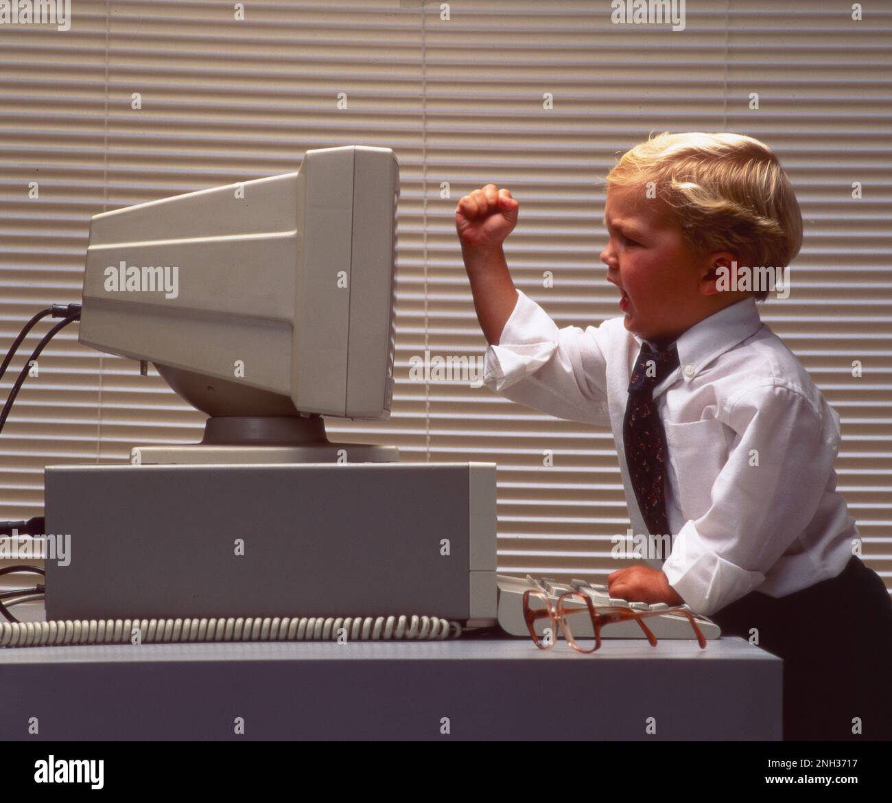 Petit garçon habillé dans une chemise d'affaires et cravate debout devant un ordinateur avec son poing serré à l'écran Banque D'Images