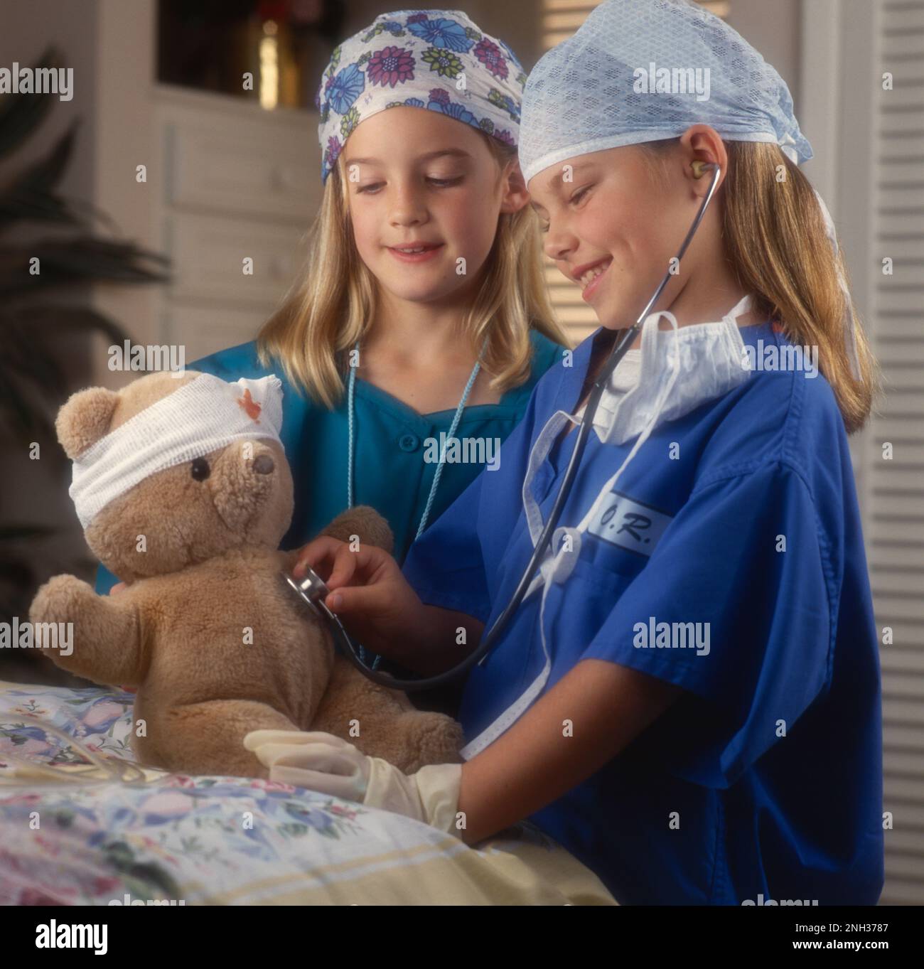 Deux jeunes filles s'habillent comme médecins, l'une avec un stéthoscope, écoutant le coeur d'un ours en peluche avec un bandage de tête Banque D'Images