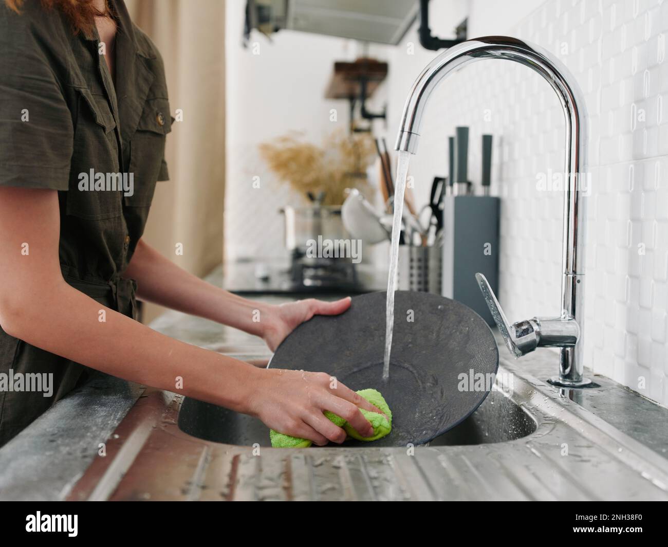 Une femme avec ses mains sans gants lave la vaisselle avec une éponge