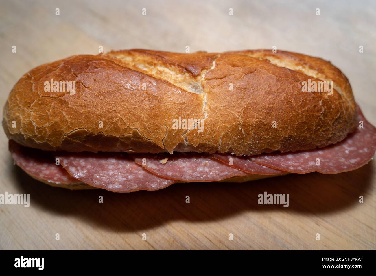 Pain de baguette croustillant avec tranches de salami sur une planche de bois Banque D'Images