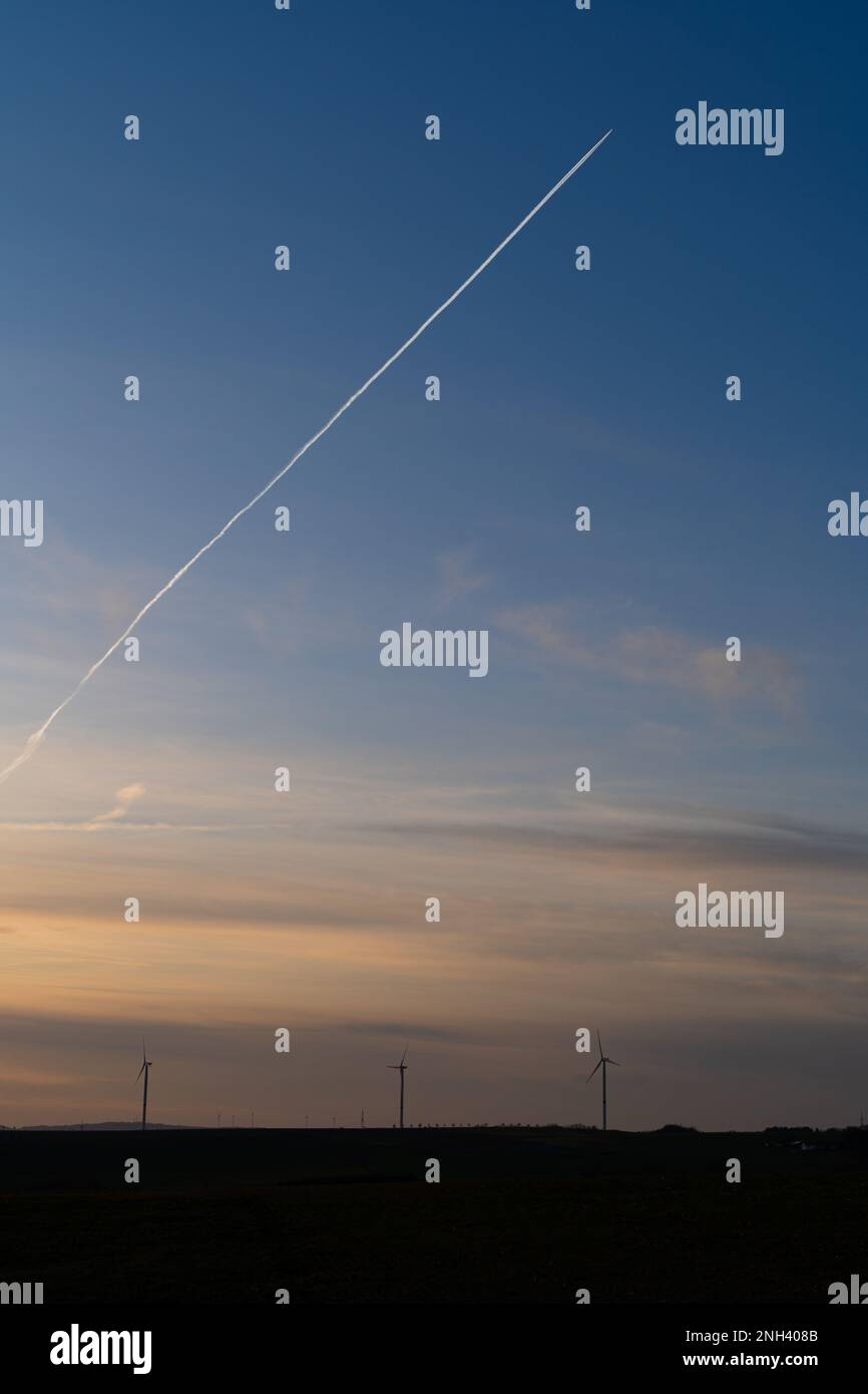 Coucher de soleil dans la campagne avec des éoliennes et un avion avec des contrailles dans le ciel bleu Banque D'Images