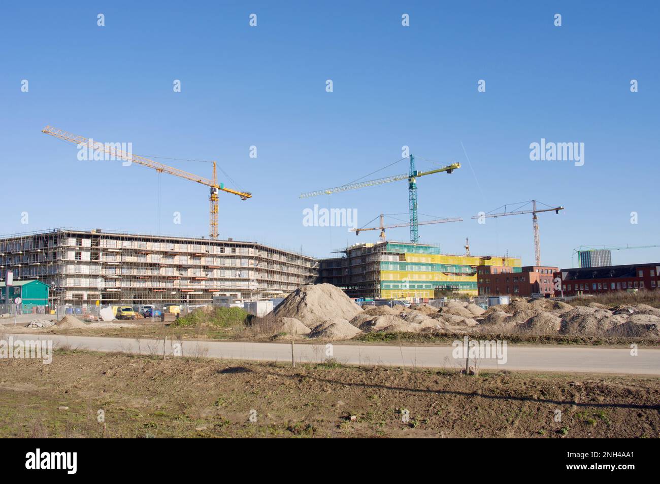 Chantier de construction avec des bâtiments en construction avec de grandes grues jaunes et vertes sur le dessus avec un ciel bleu clair Banque D'Images