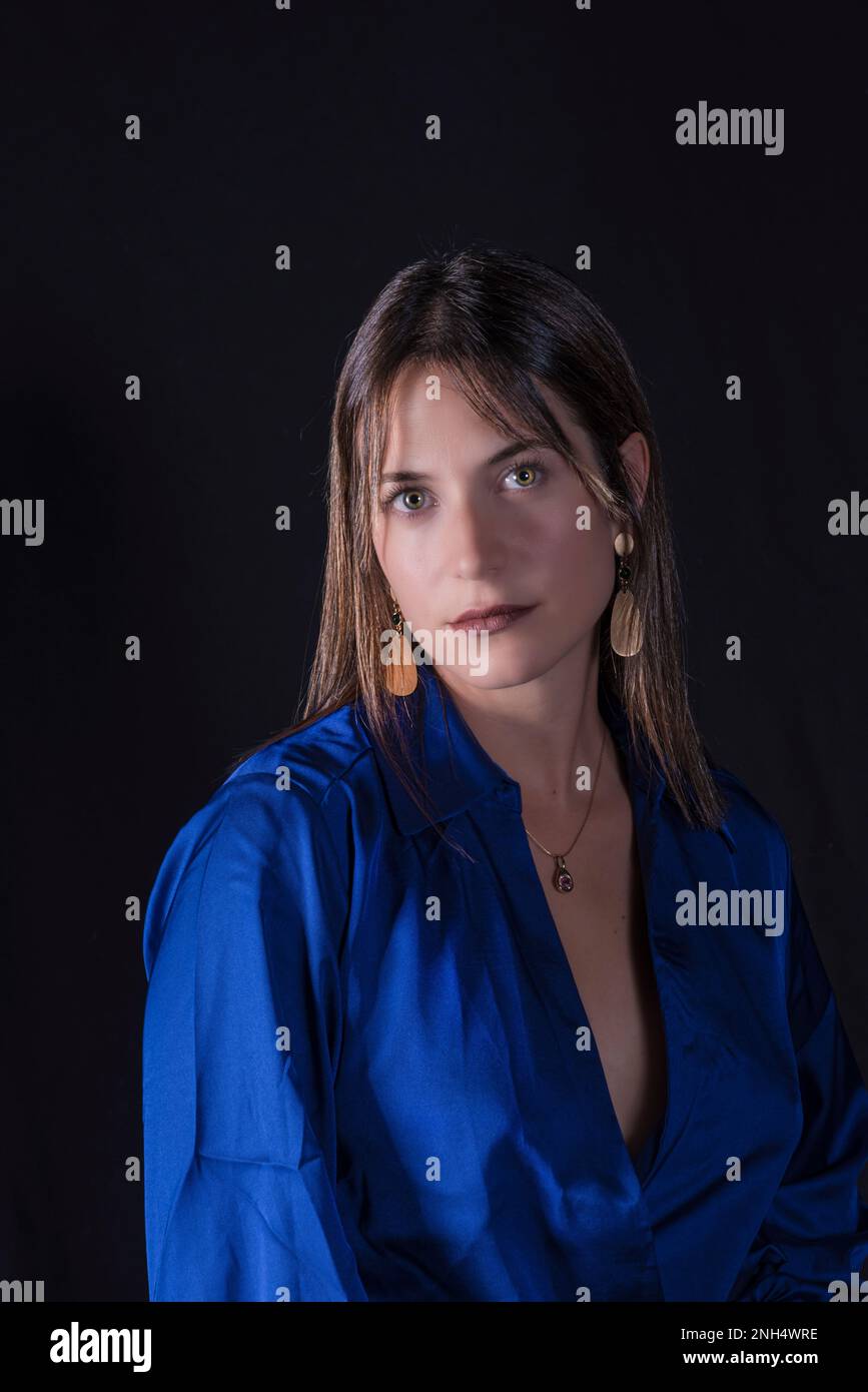 belle jeune femme vêtue de fond bleu et noir regarde droit devant avec un regard et de jolis yeux Banque D'Images