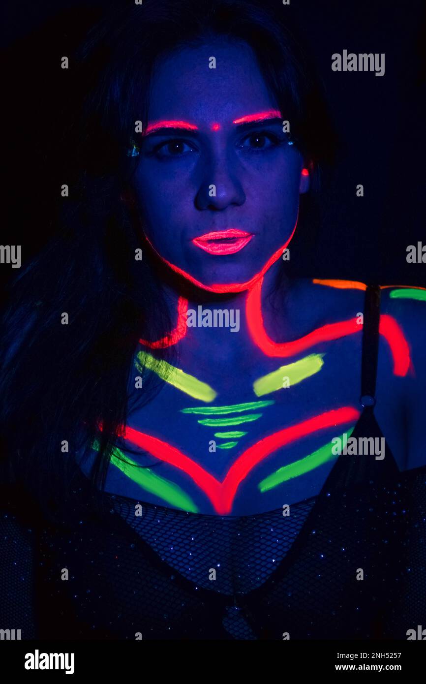 Mannequin de mode femme en lumière néon, portrait d'un beau modèle avec maquillage fluorescent, design d'art du corps en UV, visage peint, maquillage coloré, sur un b Banque D'Images