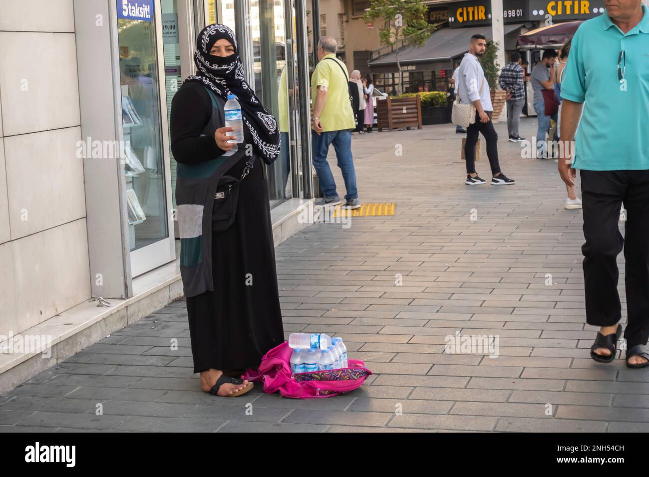 Une femme en hijab noir vendant des bouteilles d'eau dans une zone de marche près de la route, Istanbul, Turquie. Vendeurs de rue à Istanbul Turquie Banque D'Images