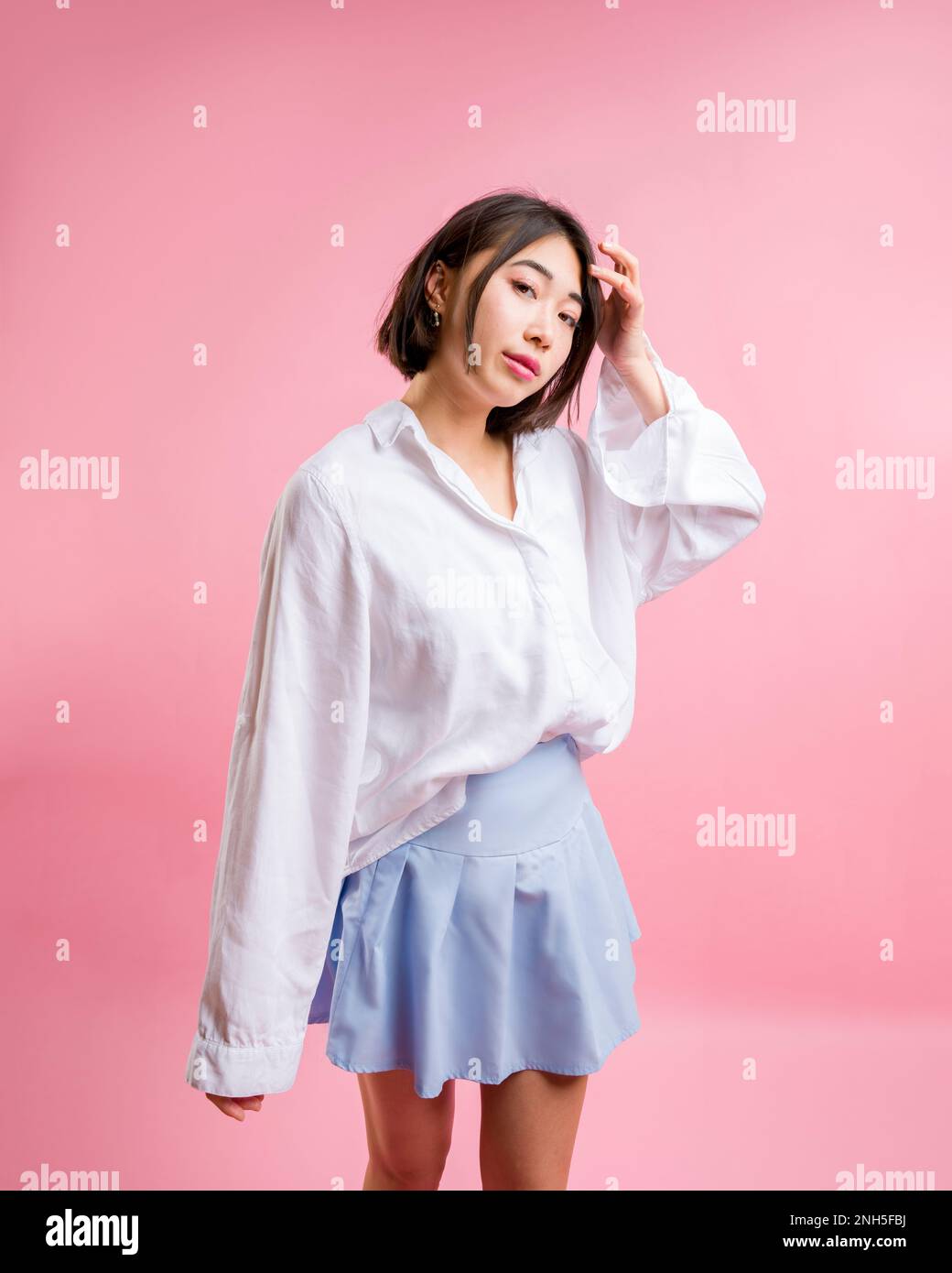3/4 Body Asian Femme debout appareil photo blanc Chemisier Bleu jupe courte face appareil photo Rose toile de fond | espace copie Banque D'Images