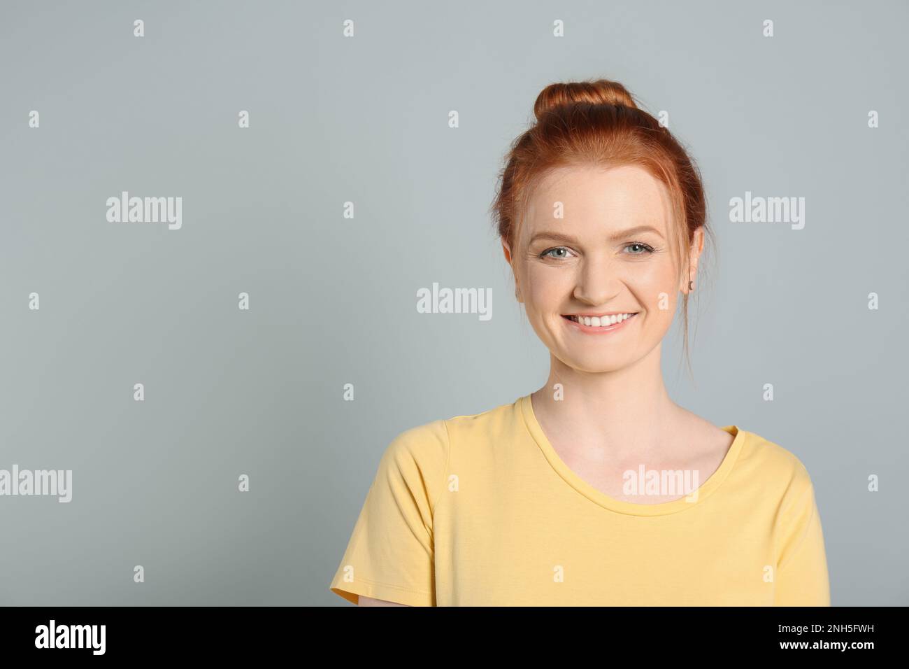 Portrait franc de la femme heureuse aux cheveux rouges avec un sourire charmant sur fond gris clair, espace pour le texte Banque D'Images