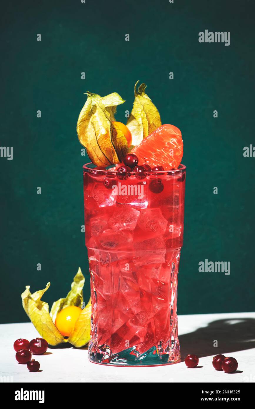 Cocktail alcoolisé brise de mer avec vodka, canneberges, jus de pamplemousse, orange et glace, décoré de physalis. Fond vert foncé, lumière dure et Banque D'Images