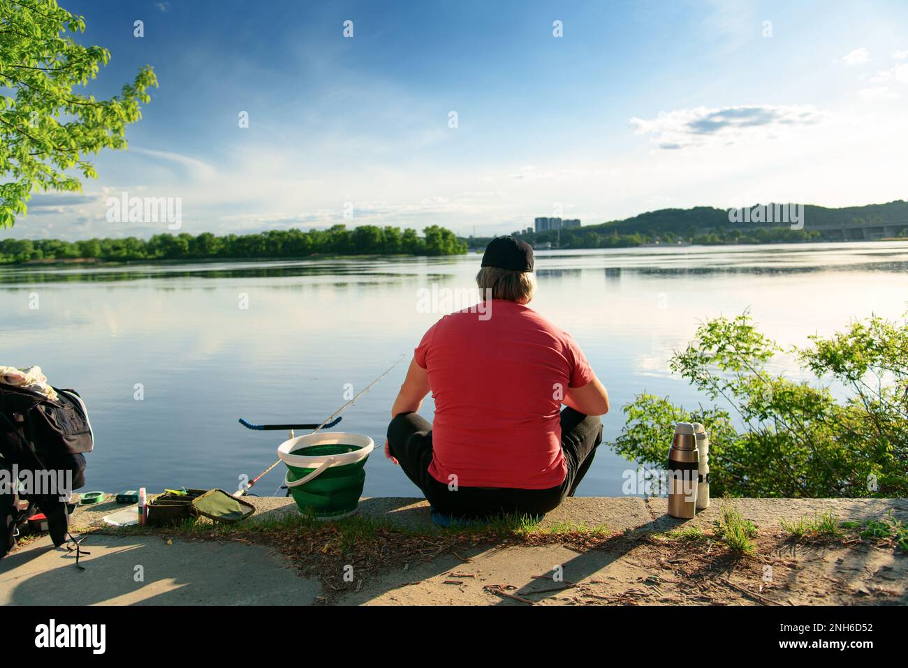 Homme assis seul près du lac calme de pêche le jour ensoleillé. Évadez-vous de la ville. Détente mentale et contemplation de la nature. Passe-temps de pêche, vacances Banque D'Images