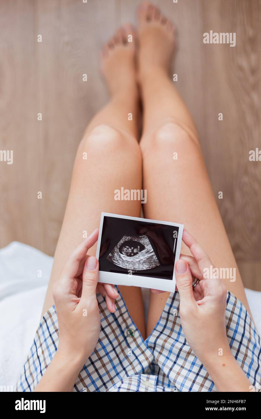 Femme en chemise assise sur le lit avec une photo échographique du bébé dans les mains. La femme attend bébé. Happy Morning confortable à la maison. Banque D'Images