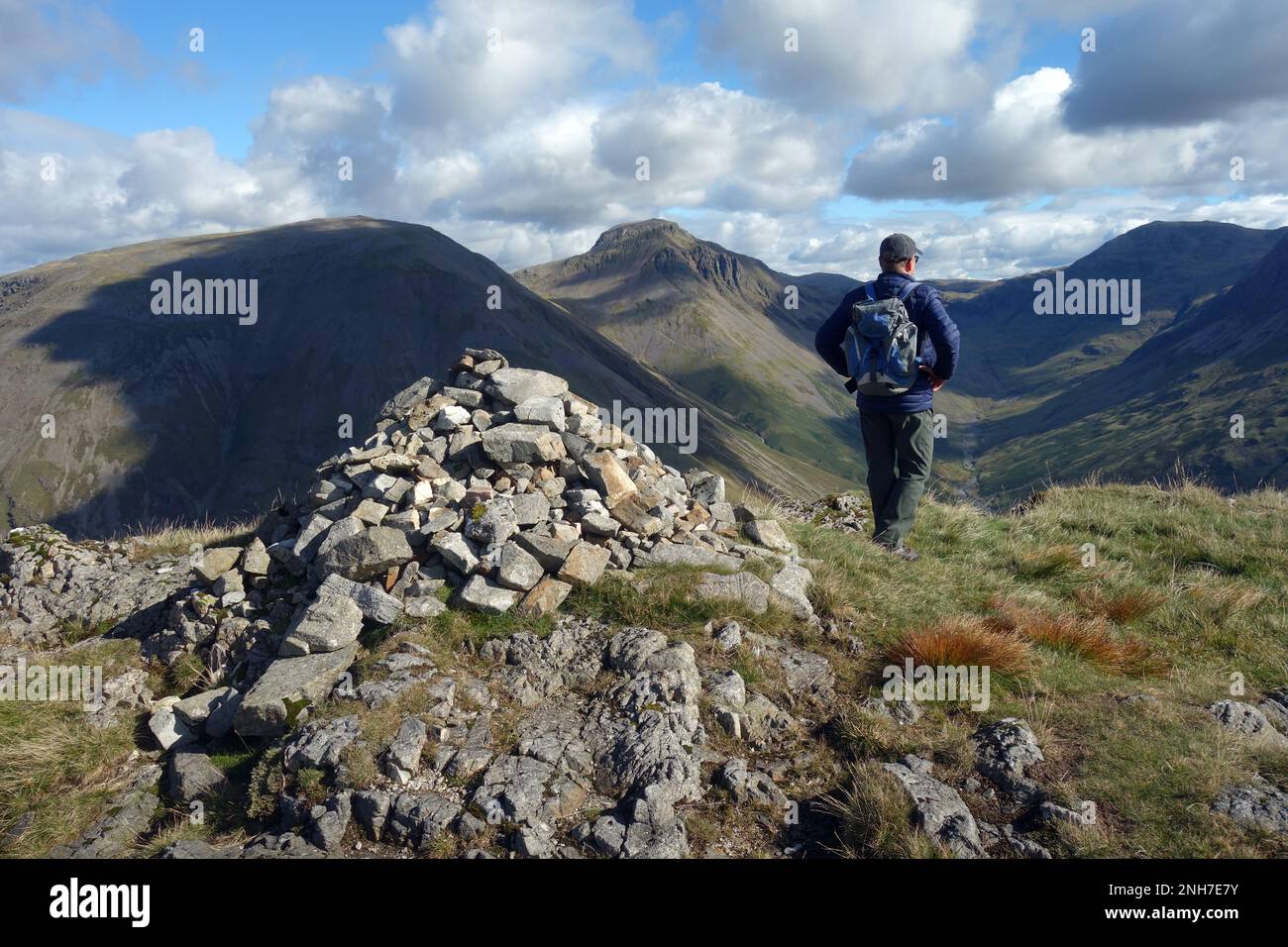 Homme (Hiker) debout par pile de pierres sur le sommet du Yewbarrow de Wainwright regardant Wasdale Head, Lake District National Park, Cumbria, Angleterre. Banque D'Images