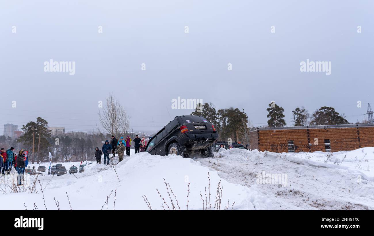 Le 4x4 de couleur noire Jeep Grand Cherokee descend d'une colline escarpée dans la neige en hiver. Banque D'Images