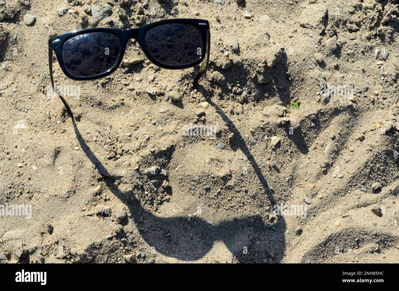 Lunettes de soleil, collées dans le sable, jetant une ombre. Banque D'Images