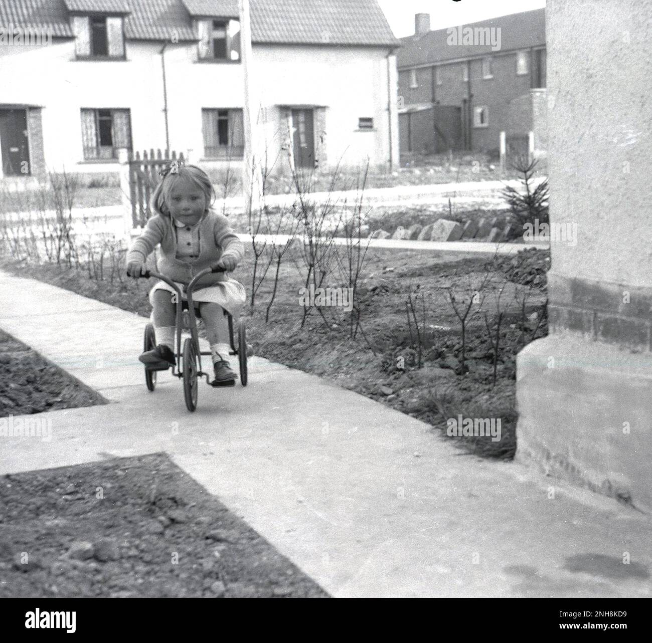 1950s, historique, un peu de doré à cheval sur son tricycle sur un chemin de béton récemment construit sur un nouveau domaine de logement, Angleterre, Royaume-Uni. Banque D'Images
