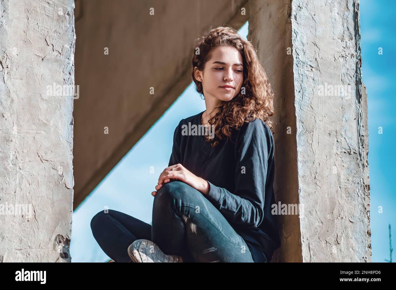 Jeune femme curieusement mignonne assise dans la fenêtre de la maison inachevée. Architecture, construction. Banque D'Images