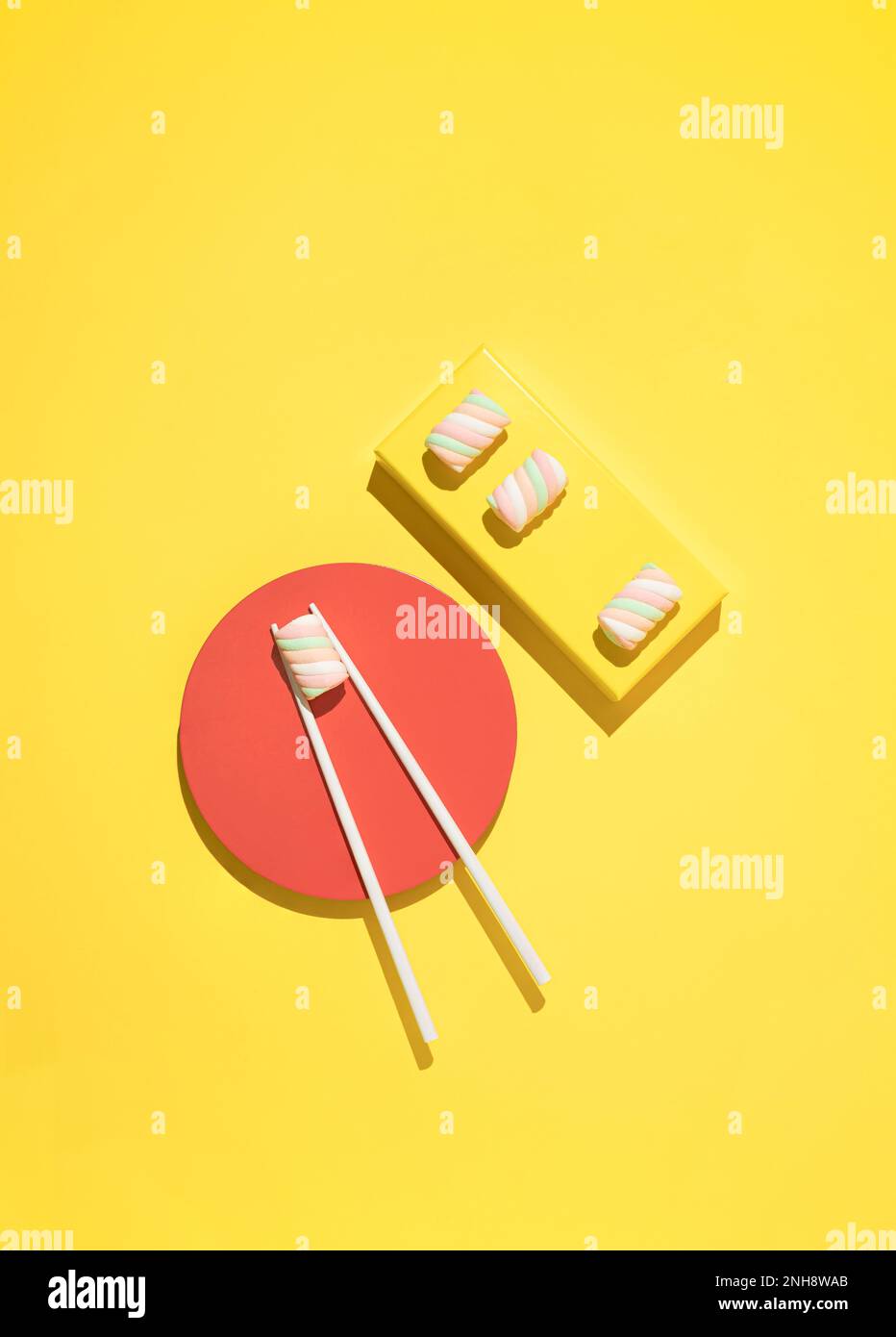 Bonbons guimauves colorés servis comme sushis avec baguettes sur fond jaune. Pose à plat. Banque D'Images