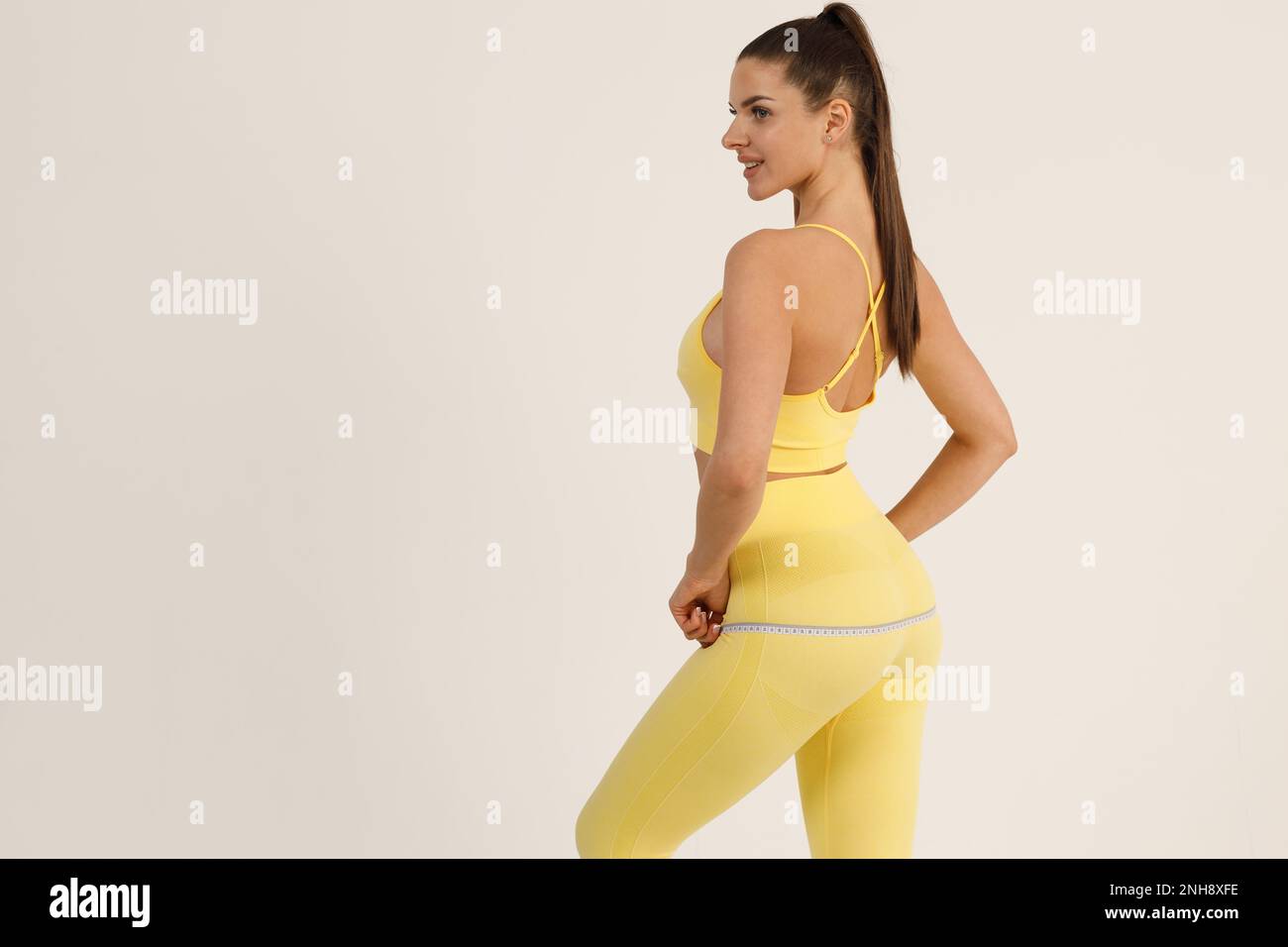Femme sportive en costume de sport jaune mesure le corps avec ruban de mesure isolé fond blanc. Banque D'Images
