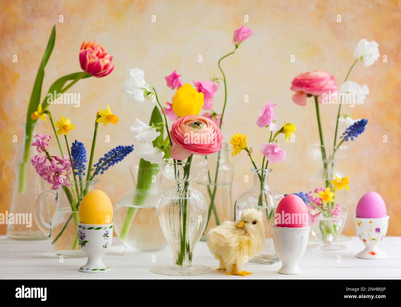 Bouquets de fleurs dans des vases en verre sur une table de Pâques festive. Œufs de Pâques colorés dans des coquetiers Banque D'Images