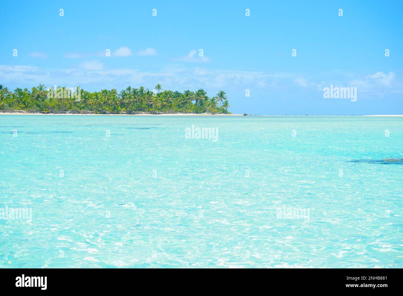 Scène tropicale typique du Pacifique Sud brume sur l'eau turquoise, cocotiers sur l'île lointaine de l'atoll bas à l'horizon ciel bleu et coulds blancs Banque D'Images