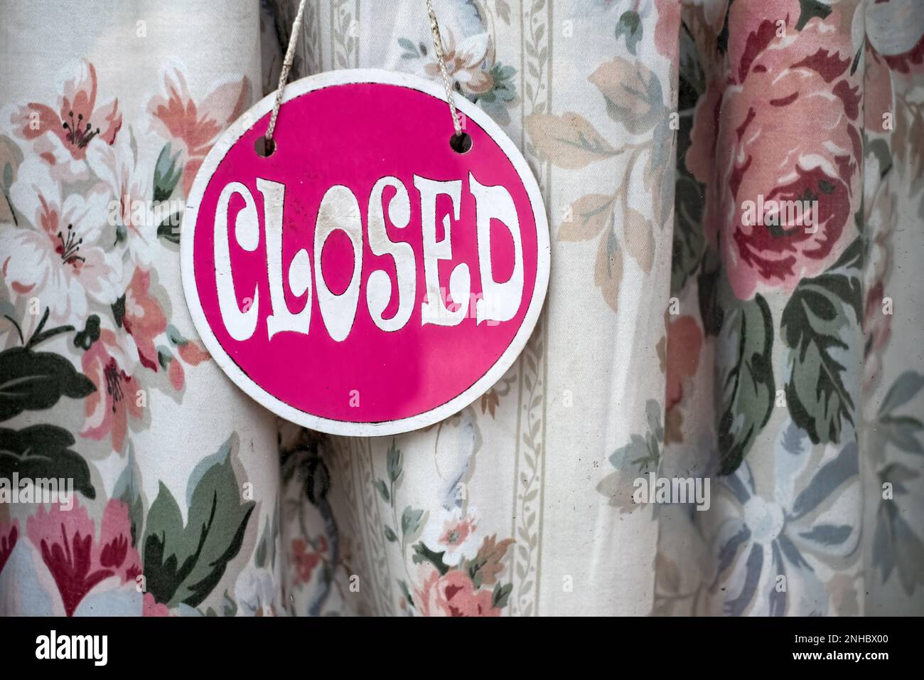 Un panneau « Désolé, nous sommes fermés » s'affiche sur une fenêtre de la porte du magasin. L'affiche est affichée devant un rideau de soleil bleuté. Il a une police rétro Banque D'Images
