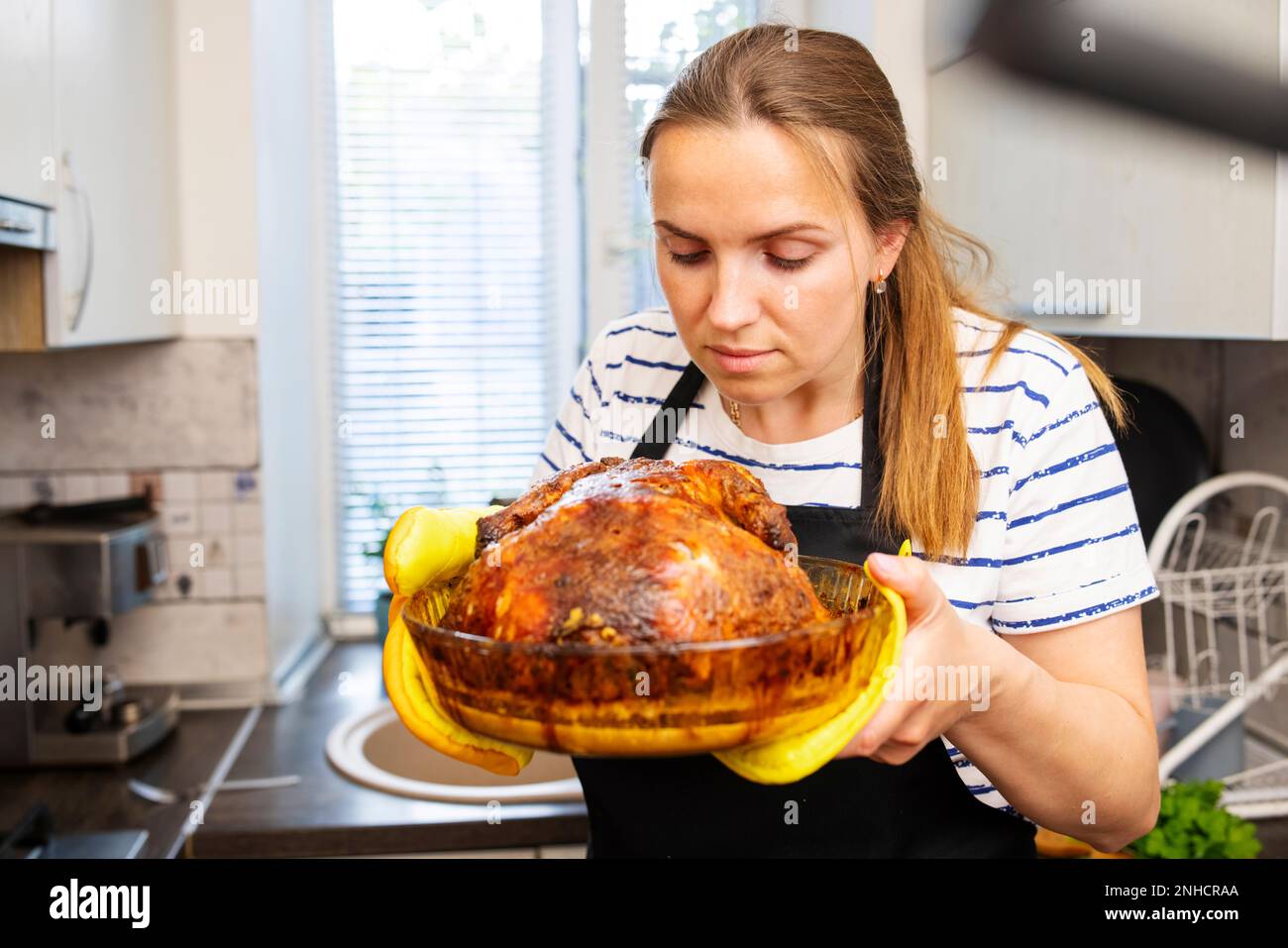 Femme en tablier noir tenant un plat avec un poulet rôti au four Banque D'Images