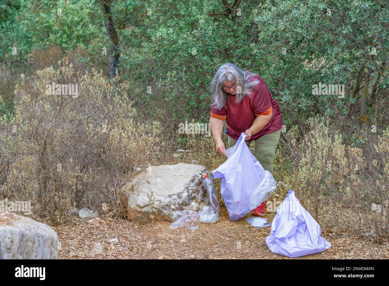Écologiste féminine adulte aux cheveux blancs, avec sacs à ordures ramassant les déchets du champ Banque D'Images