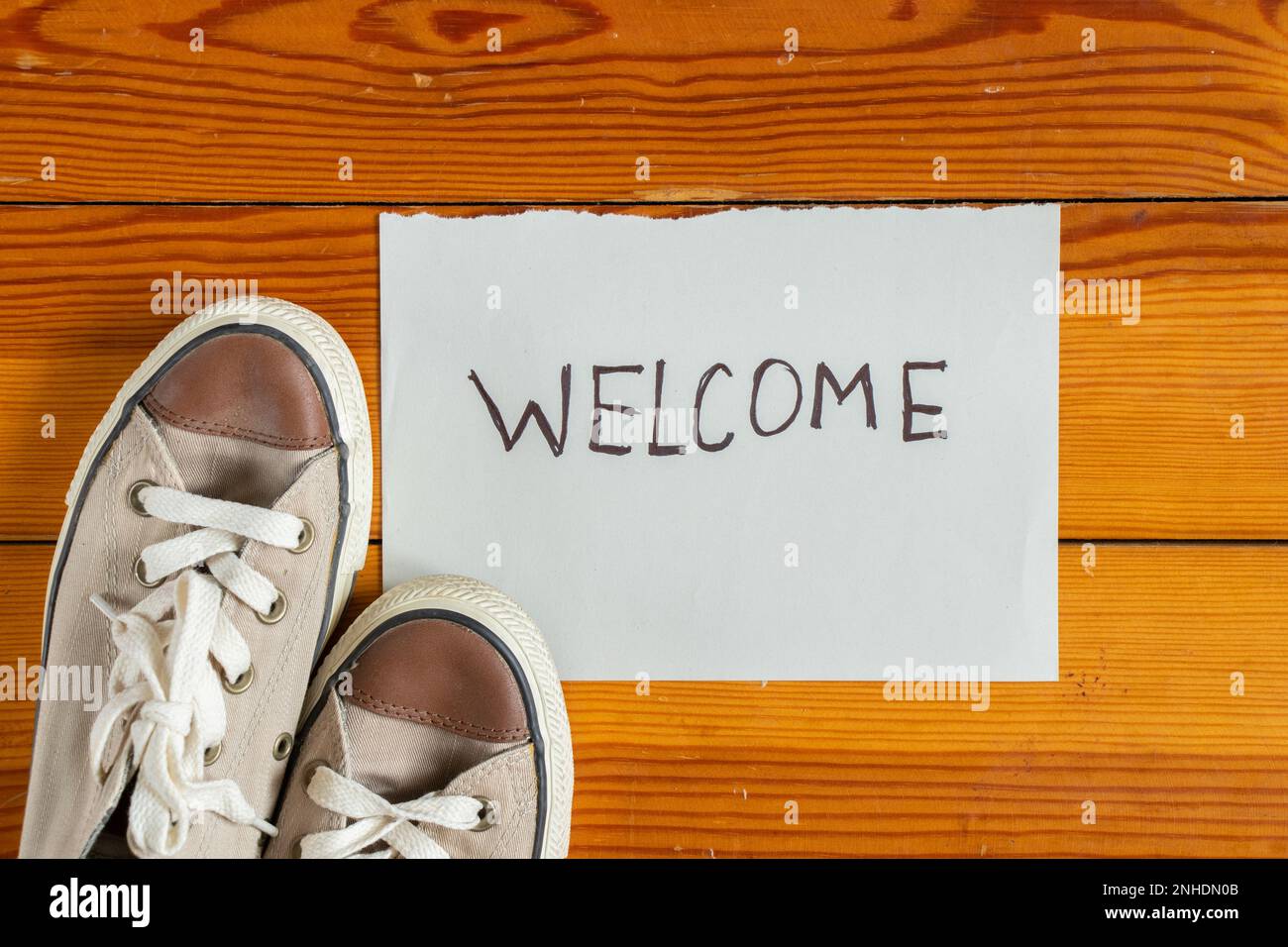 Les chaussures sont sur le plancher en bois à côté d'une feuille de papier avec les mots Bienvenue , les chaussures sont à l'entrée de la maison, salutation Banque D'Images