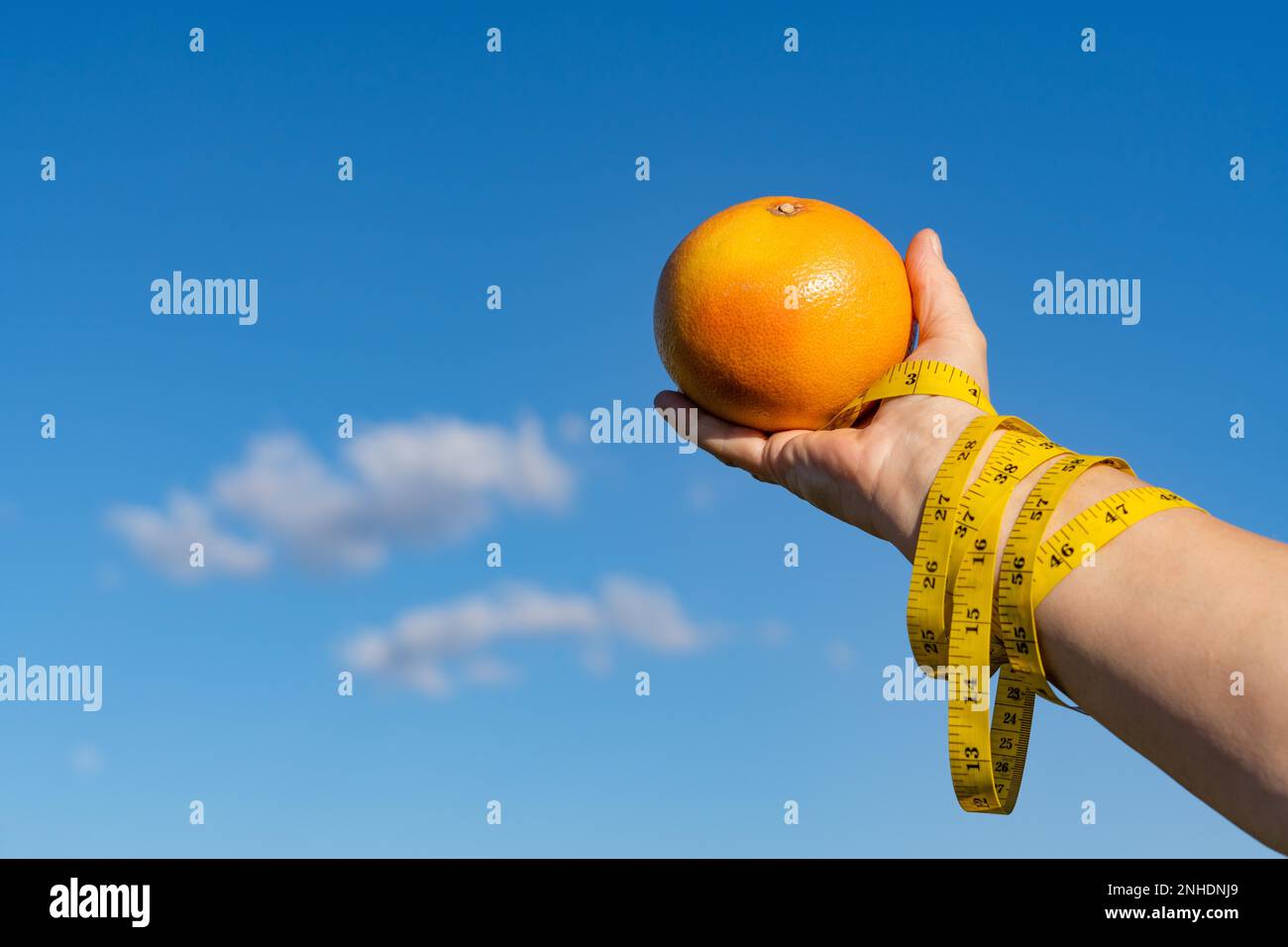 Femme tenant un pamplemousse dans ses mains avec un mètre ruban et un ciel avec des nuages en arrière-plan, concept d'un esclave de régime Banque D'Images