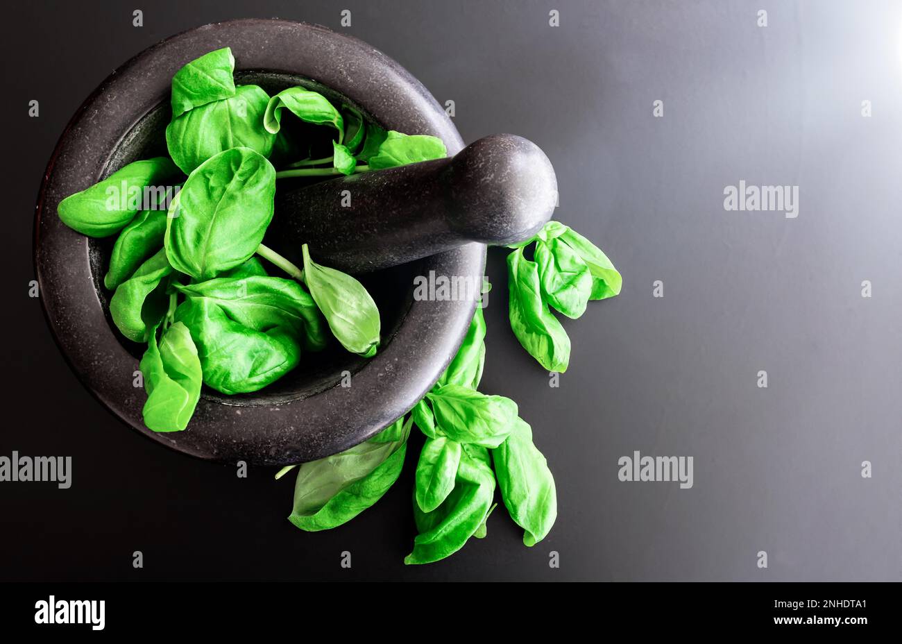Vue de dessus de feuilles de basilic frais dans la pierre Mortier avec pilon sur comptoir de cuisine sombre Banque D'Images