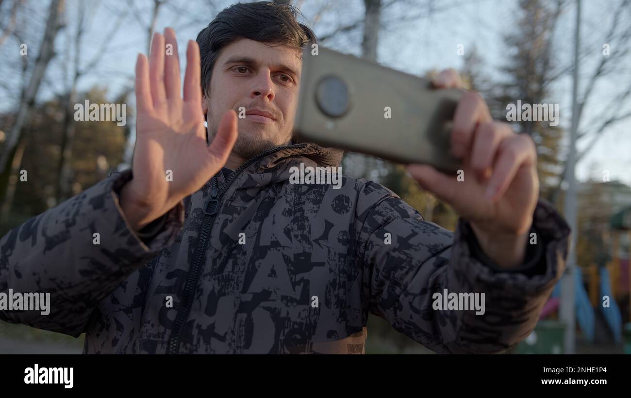 Connexion avec le monde extérieur : jeune homme tenant son smartphone horizontalement, salutation et chat vidéo avec des amis en ligne, embrassant le libre Banque D'Images