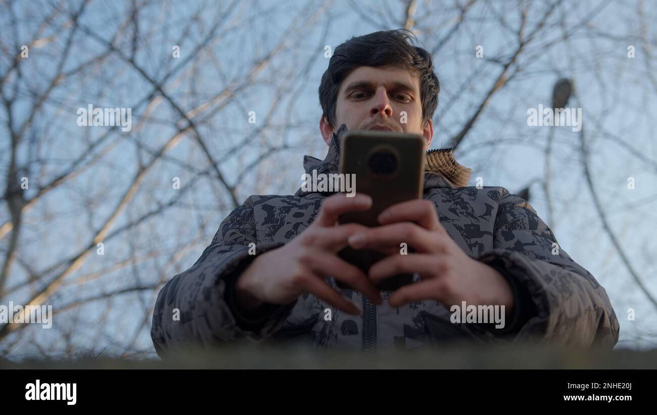 Jeune homme utilisant son smartphone pour la messagerie et les applications, vue de dessous Banque D'Images