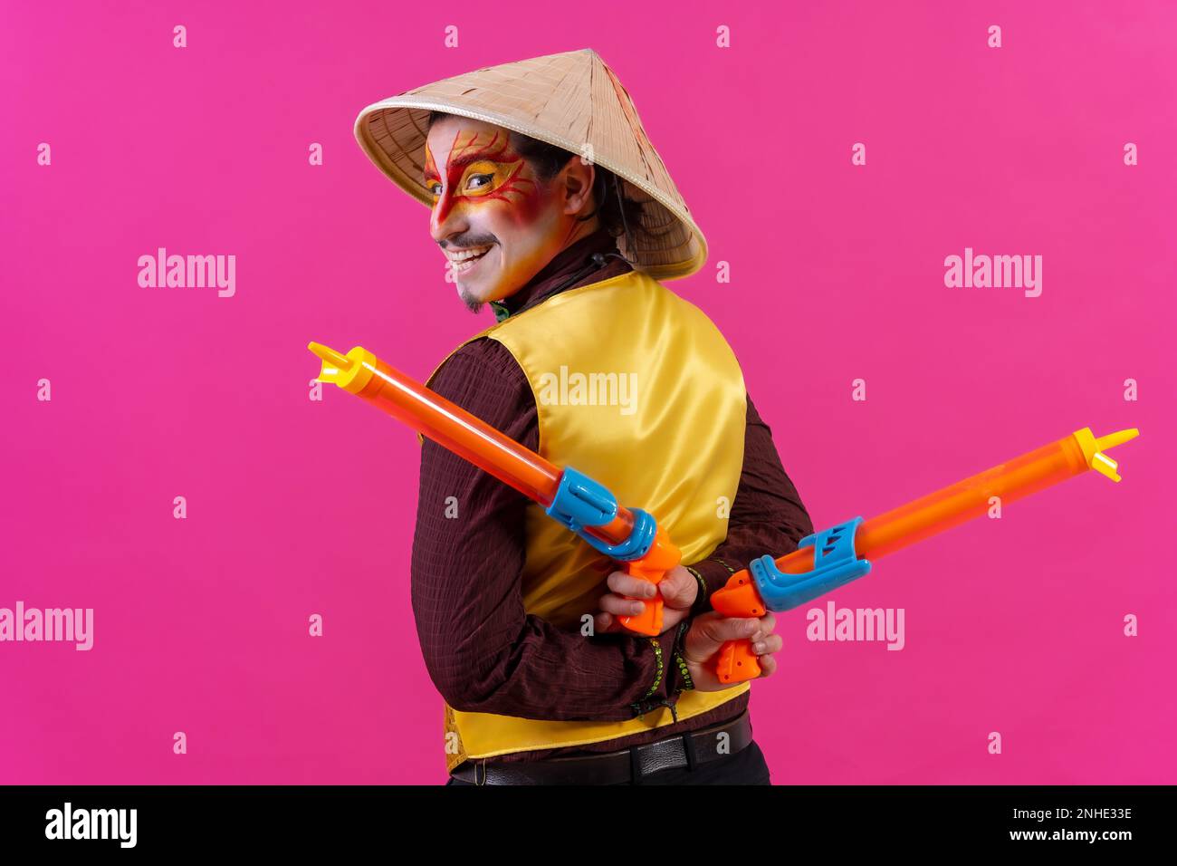Portrait d'un clown avec maquillage blanc pour le visage sur fond rose, avec des armes à feu et un chapeau chinois Banque D'Images
