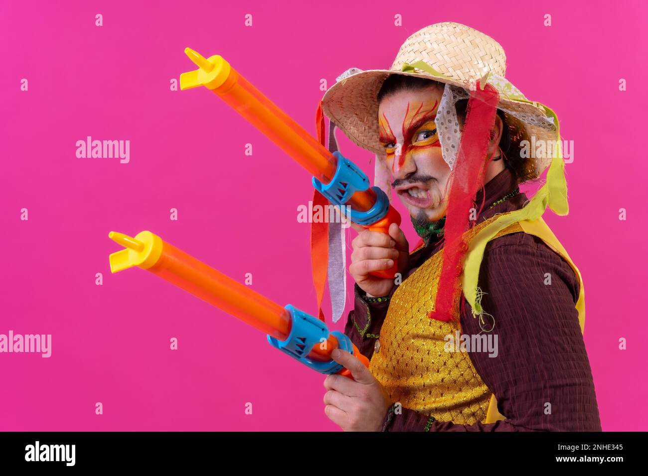 Jongleur avec maquillage blanc sur fond rose, souriant avec des armes à feu et un chapeau Banque D'Images