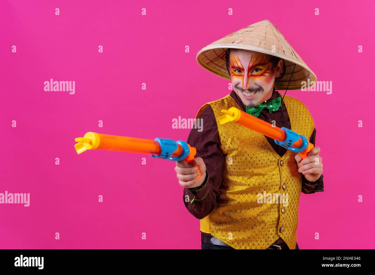 Clown avec maquillage blanc pour le visage sur fond rose, avec des armes à feu et un chapeau chinois Banque D'Images