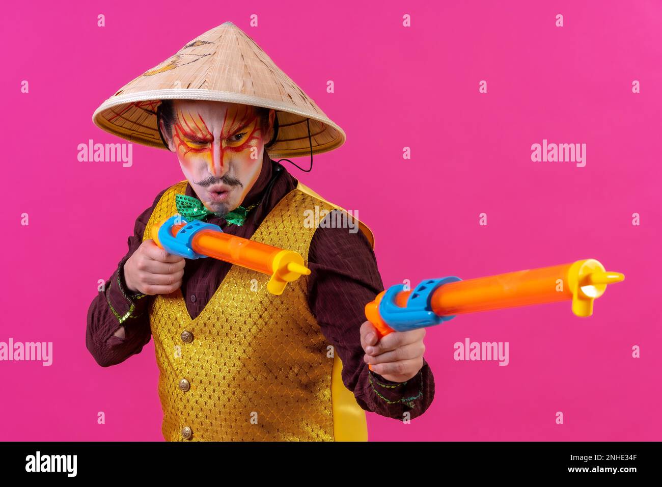 Clown avec maquillage blanc pour le visage sur fond rose, avec des armes à feu et un chapeau chinois Banque D'Images