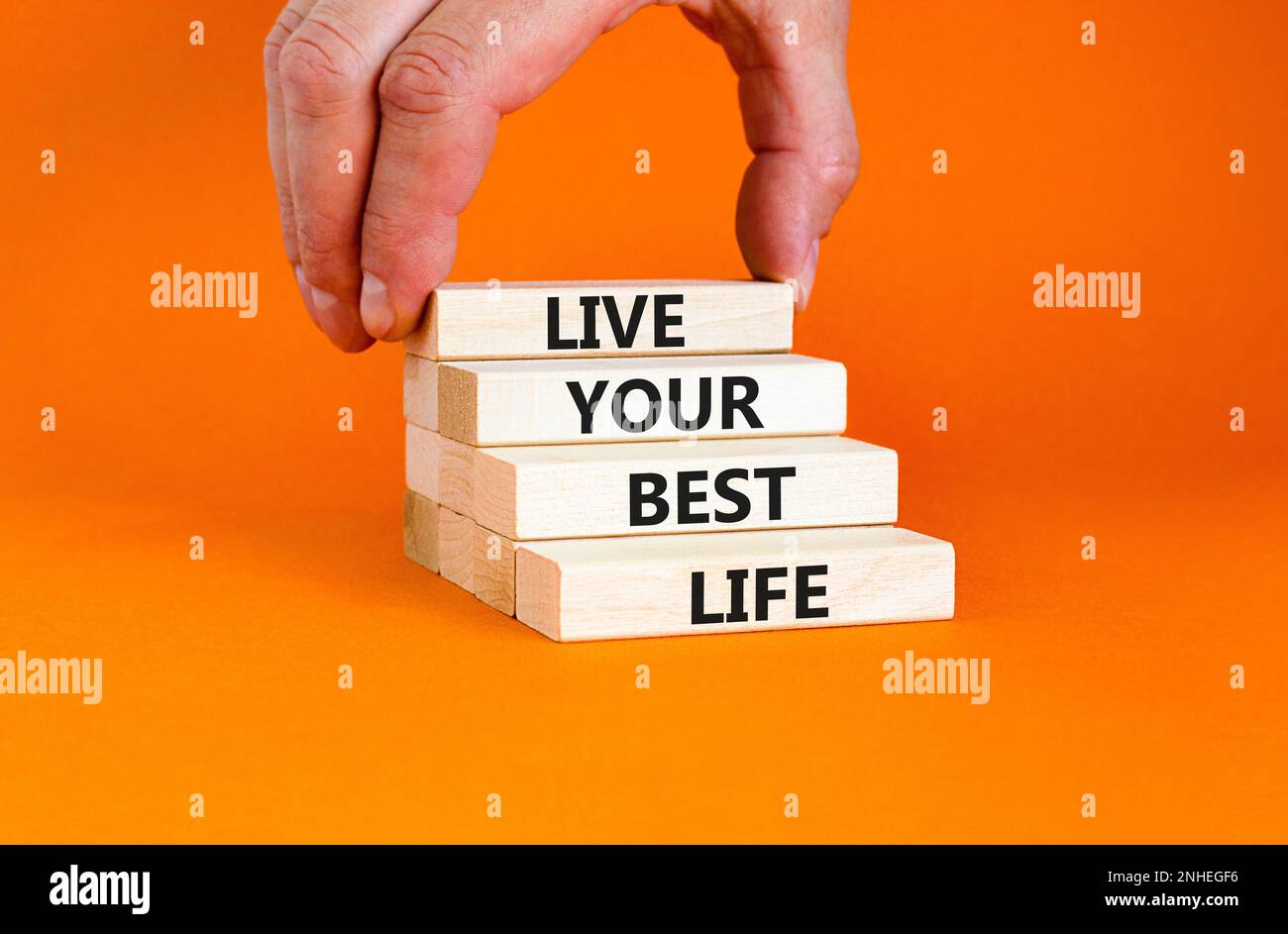 Vivez votre meilleur symbole de vie. Concept mots vivre votre meilleure vie sur des blocs de bois. Belle table orange fond orange. Main d'homme d'affaires. Affaires l Banque D'Images