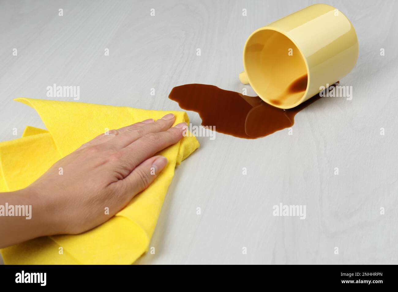 Femme nettoyant le café renversé sur une table en bois blanc, gros plan Banque D'Images