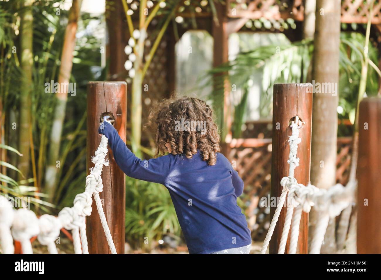 Enfant d'âge préscolaire jouant sur la corde balançoire. Magnifique jardin tropical de jardin d'enfants. Banque D'Images