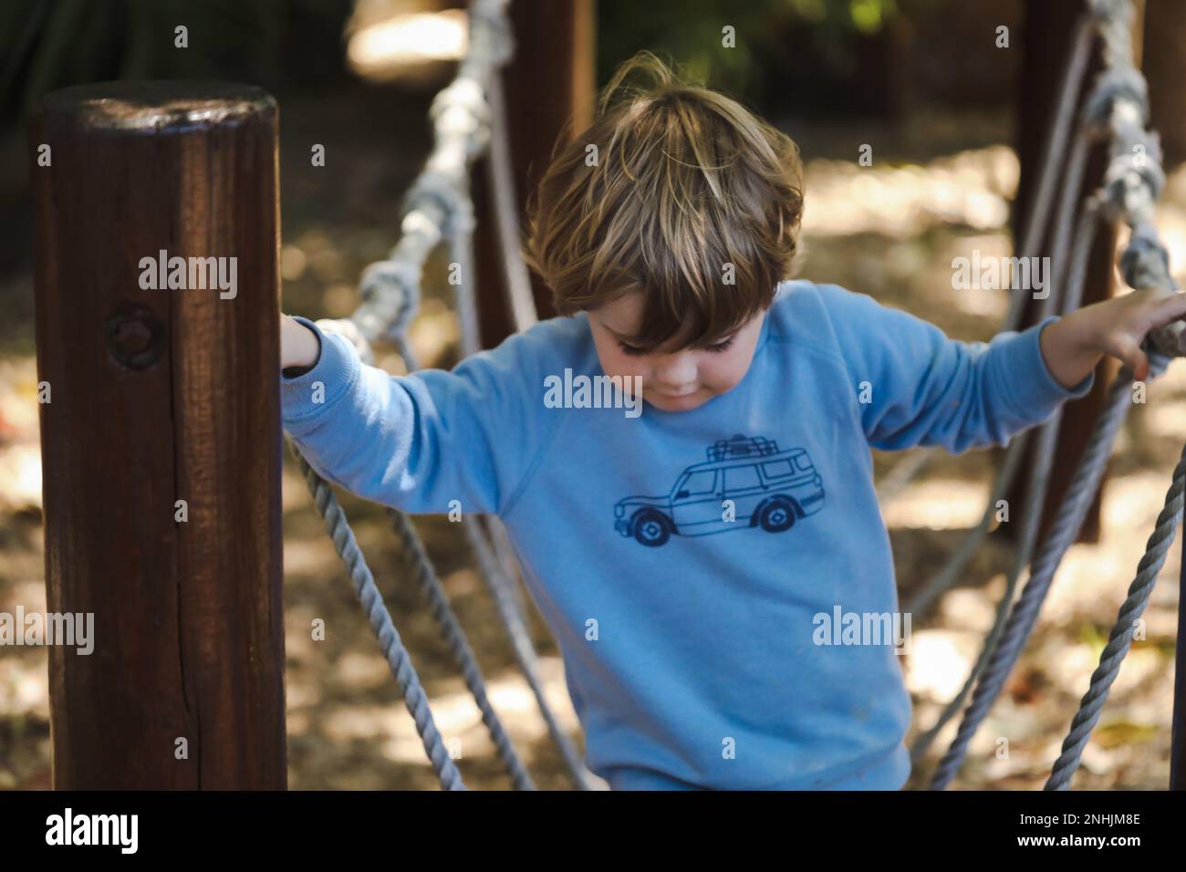 Enfant d'âge préscolaire jouant sur la corde balançoire. Magnifique jardin tropical de jardin d'enfants. Banque D'Images