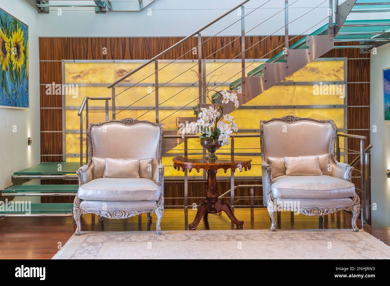 Fauteuils rembourrés en soie gris et bois et argent et escalier en acier et verre trempé sur fond nuancé avec cadre en bois exotique dans l'appartement. Banque D'Images