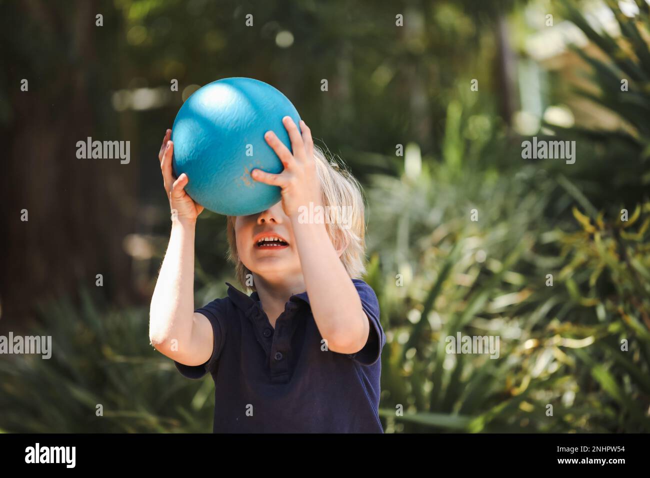 Petit garçon d'âge préscolaire jouant la capture avec la boule bleue à kindy Banque D'Images
