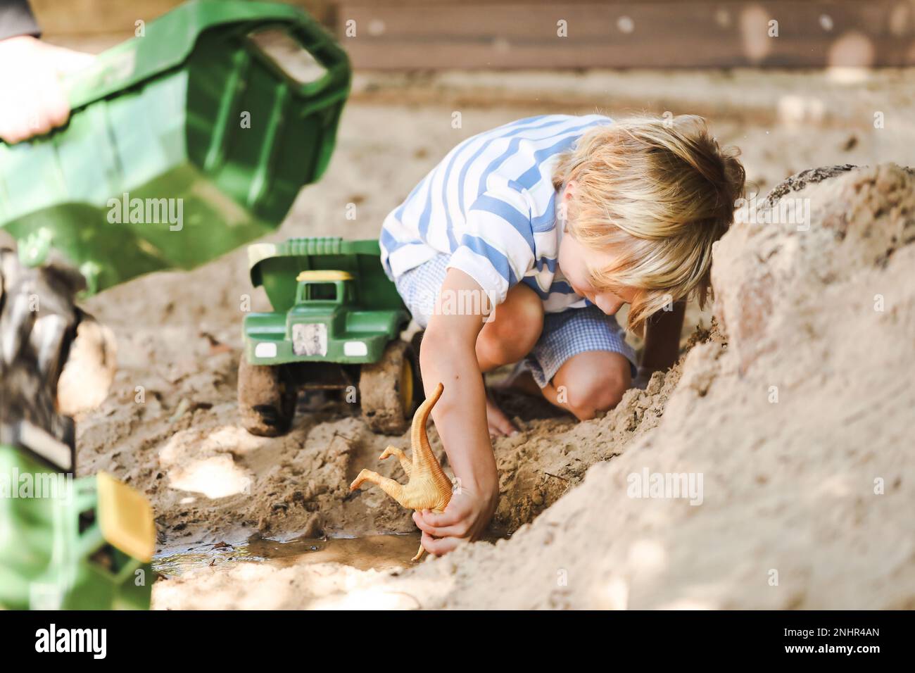 Petit garçon d'âge préscolaire jouant avec des digesteurs et des camions dans un bac à sable à kindy Banque D'Images