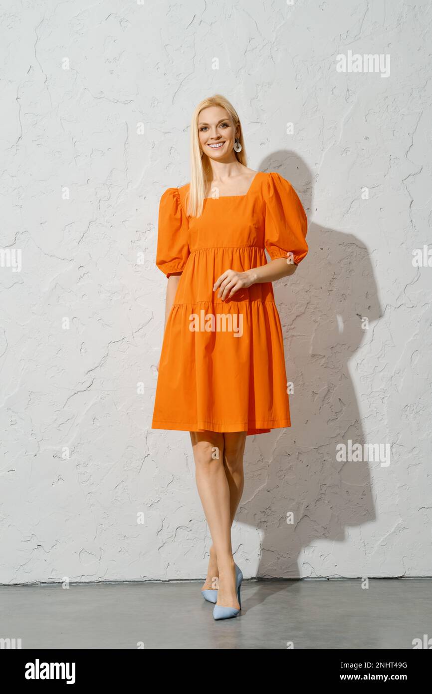 Une femme adulte souriante dans une robe de printemps orange vif marchant à l'intérieur, posant pour la caméra Banque D'Images