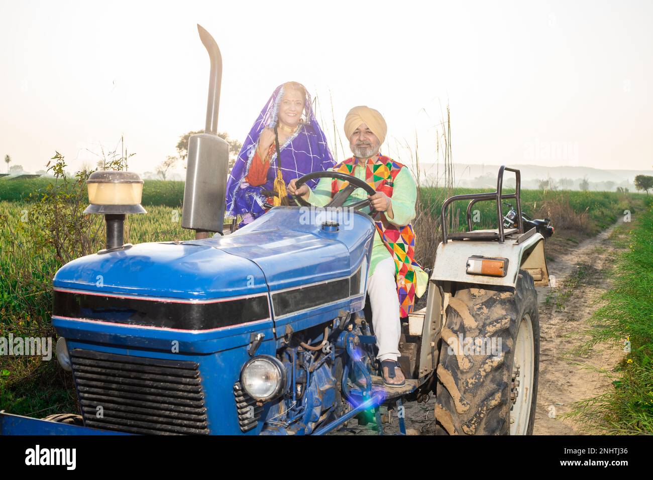 Joyeux couple de panjabi sikh senior conduisant un tracteur sur le terrain agricole en extérieur. Inde rurale. Banque D'Images