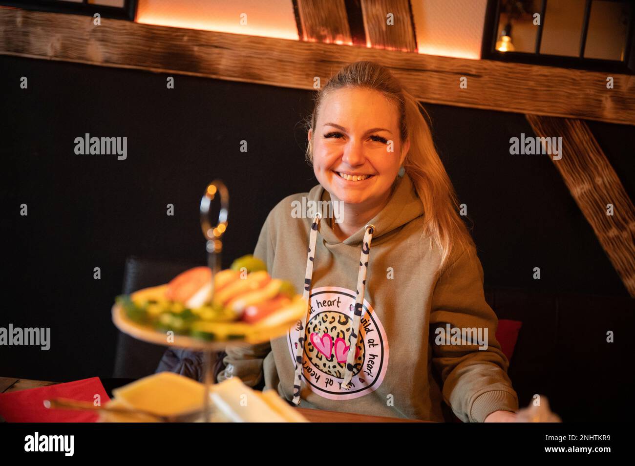 Femme souriante assise à une table de petit-déjeuner décorée avec une sélection de charcuterie et de salades saines en premier plan Banque D'Images