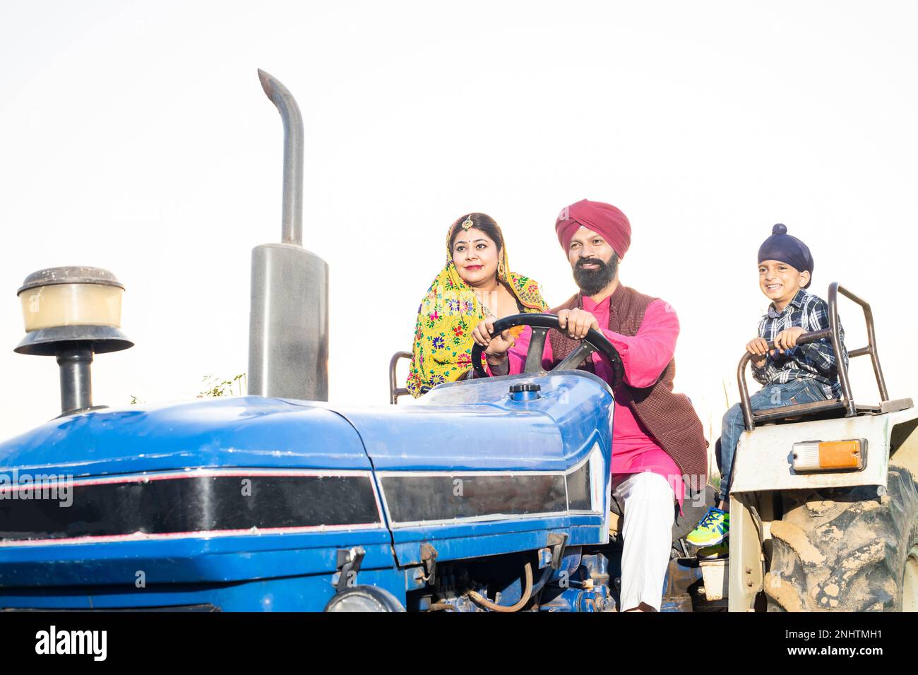 Joyeux agriculteur du punjab sikh qui conduit le tracteur le long de sa femme et de son enfant garçon à l'extérieur. Inde rurale. Banque D'Images