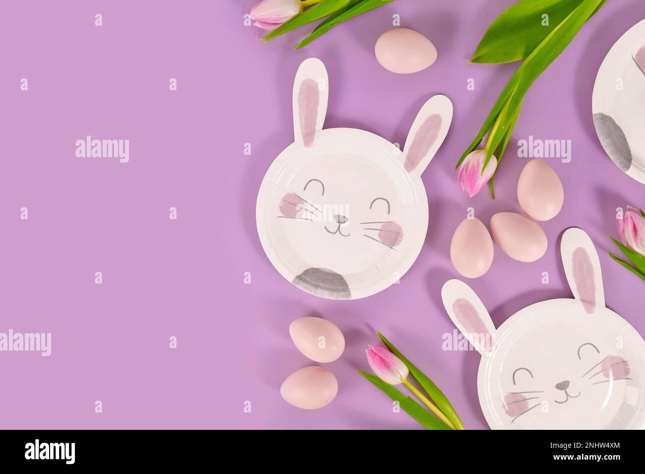 Plat de fête de Pâques avec des assiettes en papier en forme de lapin, des œufs et des fleurs de tulipe sur fond violet avec espace de copie Banque D'Images
