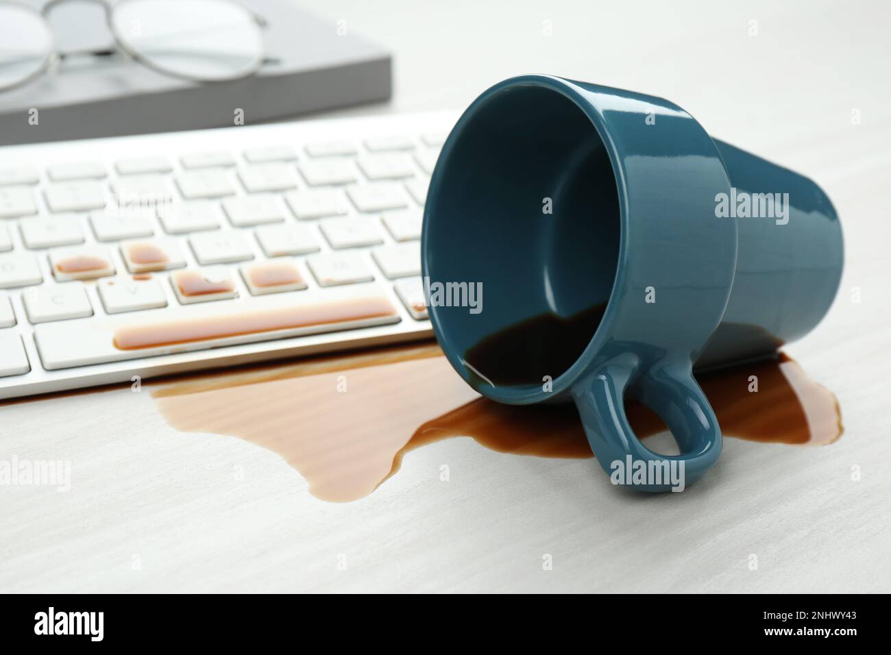Tasse de café renversée sur le clavier de l'ordinateur sur une table en bois blanc Banque D'Images Tasse de café renversée sur le clavier de l'ordinateur sur une table en bois blanc Banque D'Images